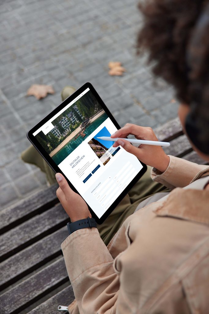 Frau sitzt auf Parkbank und nutzt den digitalen Meldeschein auf ihrem Tablet
