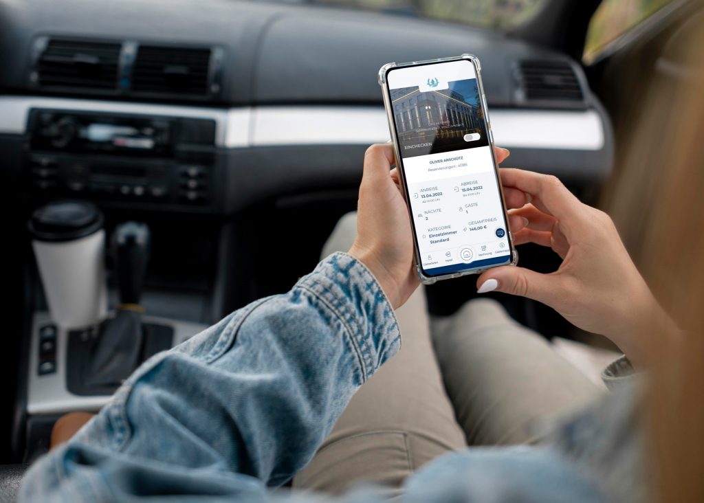 Frau sitzt im Auto mit Smartphone in der Hand, auf welchem die SoftTec hotline Gäste-App zu sehen ist.