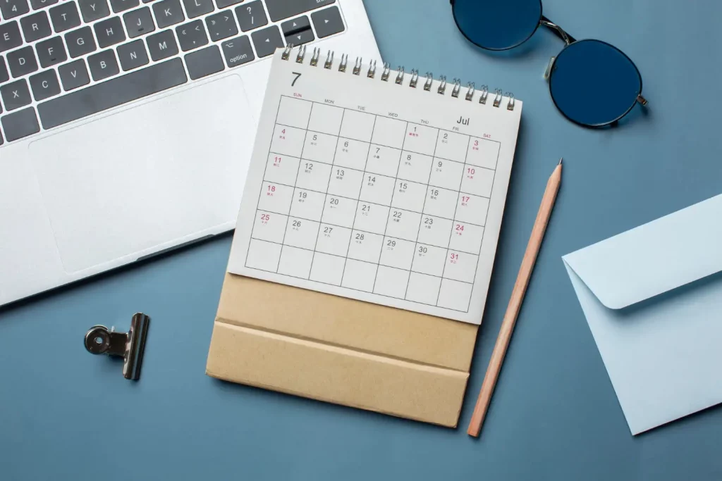Kalender, Schreibutensilien, Sonnenbrille und Laptop liegen auf dem Schreibtisch