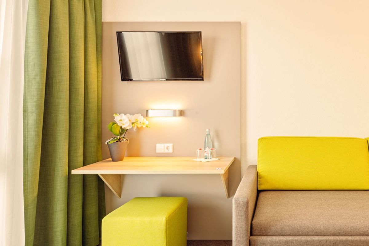 Sitzecke im Hotelzimmer des Highway Hotel Herbolzheim mit Schreibtisch, Orchidee und Schlafsofa