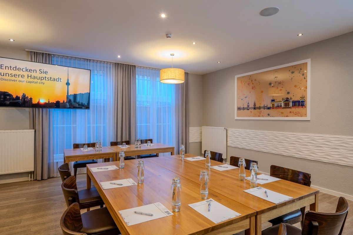 Meetingraum im Businesshotel Berlin mit langem Holztisch, Bildschirm und Wandbild des Reichstags